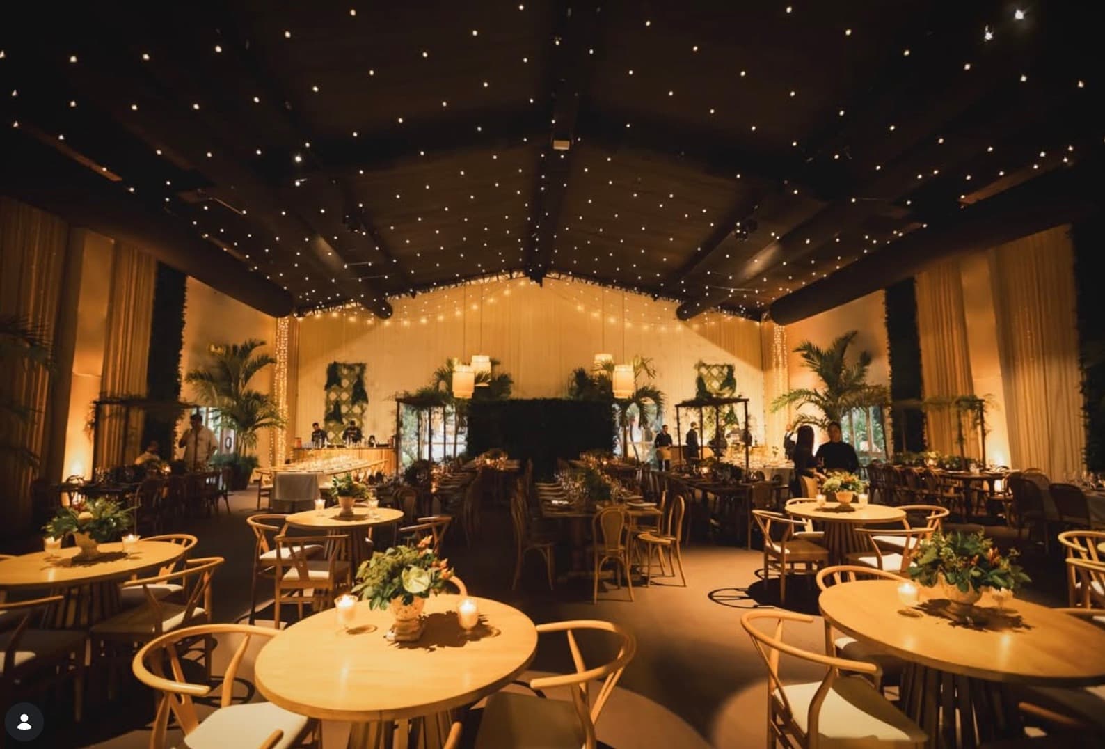 Salón de eventos con mesas redondas, luces cálidas y cielo de estrellas