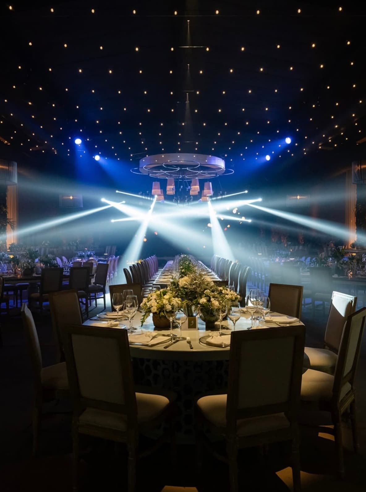 Mesa de cena con iluminación azul, arreglos florales y cielo de estrellas