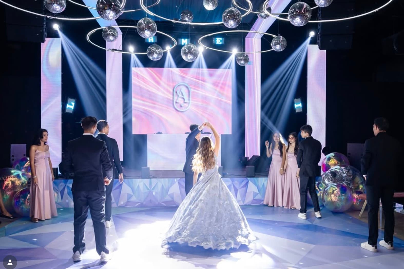 Novios bailando en una pista iluminada con invitados alrededor